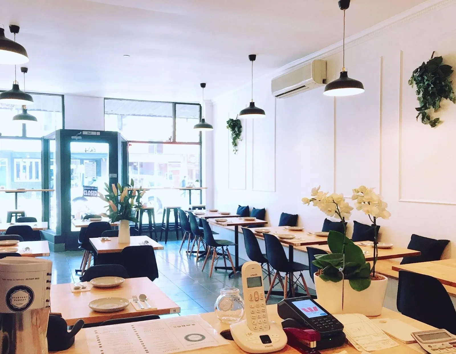 The bright Everyday's Sunday dining room — white walls, timber tables and orchids.